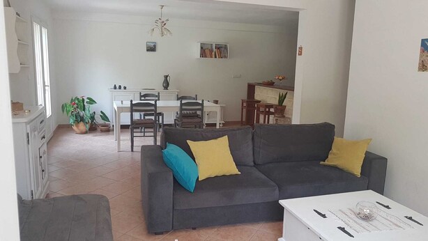 A living room with a grey sofa, two yellow cushions, a white coffee table, and a dining area with a white table and chairs. - Rez-de-villa (LE BEAUSSET)