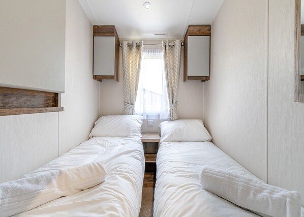 A narrow room with two beds, wooden headboards, and a window with curtains.