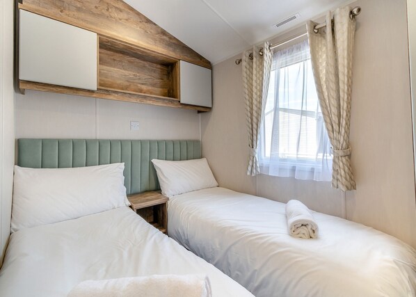 A double room with two beds, a wooden headboard, a window with curtains, and a mirror above the beds.