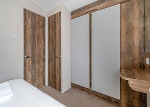 A bedroom with a bed, two wooden doors, a wardrobe, and a wooden shelf.