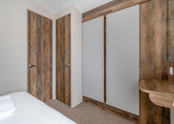 A bedroom with a bed, two wooden doors, a wardrobe, and a wooden shelf.