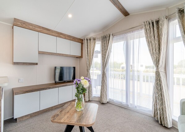 Una habitación moderna con televisión, banca de madera y un florero con flores.