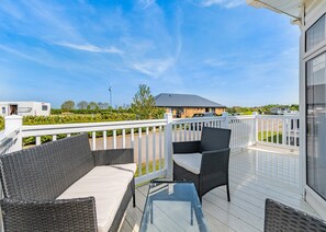 A balcony with wicker furniture, a glass table, and a view of a caravan park.