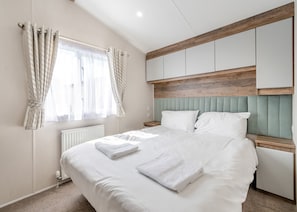 Un dormitorio con cama, cortinas, radiador, cabecero de madera y mesita de noche.