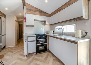 A compact kitchen with a gas stove, oven, sink, and a window.