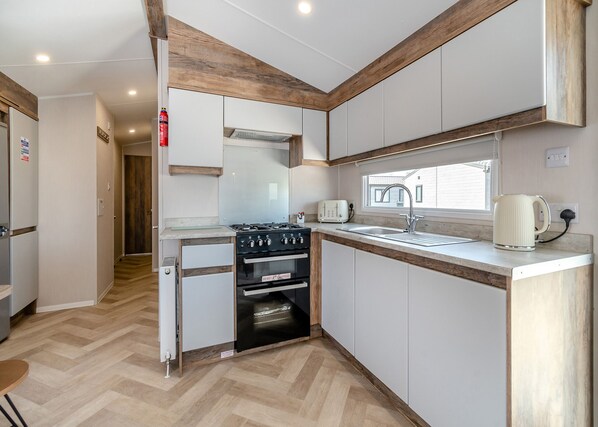A compact kitchen with a gas stove, oven, sink, and a window.