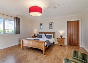 Ein Schlafzimmer mit einem hölzernen Bett, Nachttischen, einer roten Pendelleuchte, einer Holztür und einem Fenster mit Vorhängen.