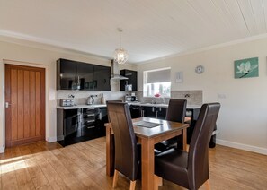 A modern kitchen with black cabinets, a wooden dining table, and a pendant light.