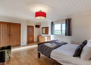 A bedroom with a bed, a wooden wardrobe, a television, and a window with curtains.