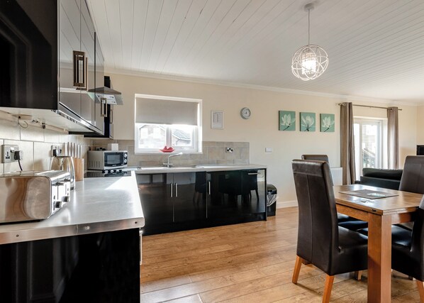 Una cocina moderna con una isla central, un comedor con mesa y sillas de madera, y un ventanal con cortinas.