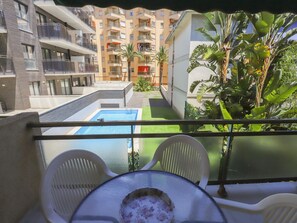 En balkon med pool, hvide stole og et bord.