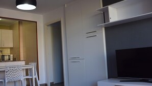 A modern kitchen with white cabinets, a dining area with a glass table, and a flat-screen TV on a white stand. - Cozy Apartment with Terrace Near Capellans Beach, Salou (Salou)
