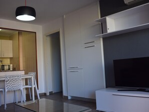 A modern kitchen with white cabinets, a dining area with a glass table, and a flat-screen TV on a white stand.