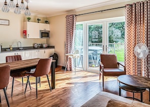 A modern kitchen with a microwave, sink, and cabinets. There is a dining area with a wooden table and chairs. A sliding glass door leads to an outdoor patio with a table and chairs.