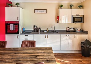A modern kitchen with a built-in oven, microwave, and toaster, a wooden dining table, and a trash bin.