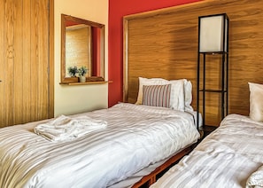 A hotel room with two beds, a wooden wardrobe, a mirror, and a bedside table with a plant.