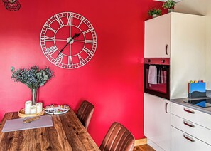 A red-walled room with a wooden dining table, chairs, a white cabinet, and a wall clock.