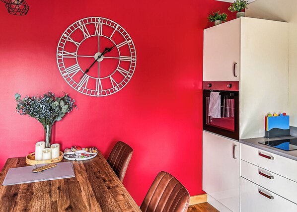 A red-walled room with a wooden dining table, chairs, a white cabinet, and a wall clock. - 3 bedroom accommodation in Flaxton (Flaxton)