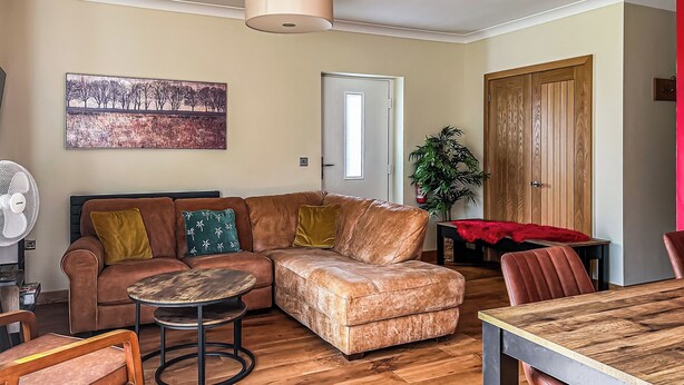 A living room with a sectional sofa, a round coffee table, a dining table with chairs, a fan, a painting, a door, and a wooden cabinet. - 3 bedroom accommodation in Flaxton (Flaxton)