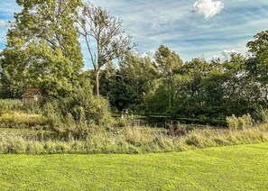 A grassy field with a small wooden structure, surrounded by trees and a pond.