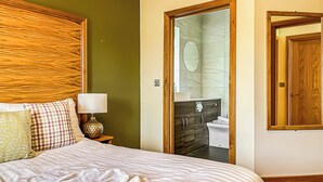 A hotel room with a bed, a nightstand, a lamp, a bathroom visible through an open door, and a wooden-framed mirror. - 3 bedroom accommodation in Flaxton (Flaxton)