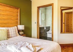 A hotel room with a bed, a nightstand, a lamp, a bathroom visible through an open door, and a wooden-framed mirror.