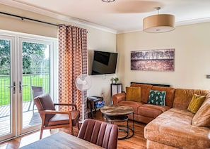 A living room with a sofa, chairs, a TV, a fan, and a painting.