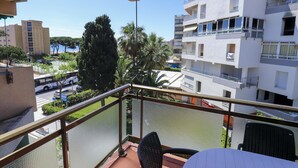 Un balcón con vista a una zona residencial, que incluye un edificio de varios pisos y vehículos estacionados.