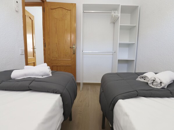 Habitación de hotel con dos camas, una puerta de madera, un armario blanco y una toalla blanca sobre cada cama.