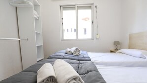 Habitación de hotel con dos camas, una ventana, una mesita de noche y un armario.