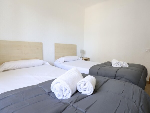 A hotel room with two beds, each with a wooden headboard, and a small bedside table with a lamp.