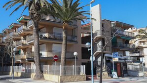 Un edificio residencial de varios pisos con balcones, palmeras y una señal de prohibido el acceso.