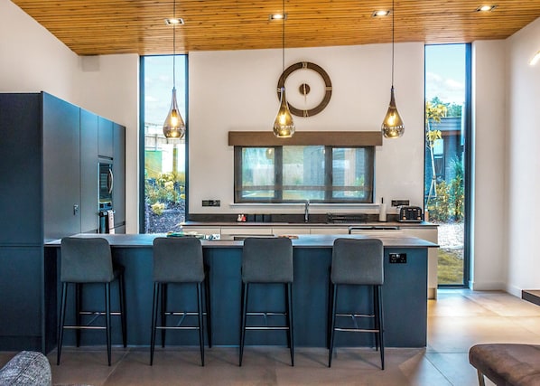 Uma cozinha moderna com ilha central, banquetas, luminárias pendentes e uma janela grande.