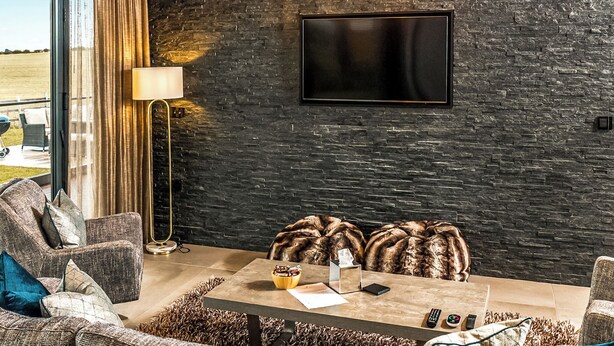 A modern living room with a stone wall, a flat-screen TV, and a sofa with decorative pillows. - Three bed lodge with two king-size beds and one twin (king by arrangement). (Nottingham)