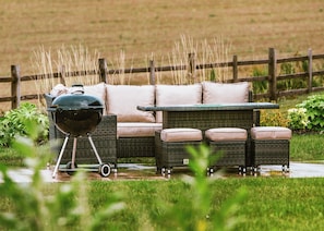 A patio with a grill, wicker furniture, and a cushioned sofa.