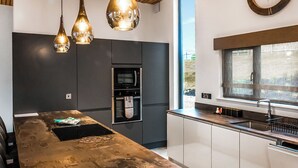 A modern kitchen with a large island, stainless steel appliances, pendant lighting, and a window providing natural light. - Three bed lodge with two king-size beds and one twin (king by arrangement). (Nottingham)