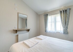 A bedroom with a bed, a mirror, a radiator, and a window with curtains. - Brand new for 2021. Outstanding, spacious lodge with one double and two twin. (Skegness)