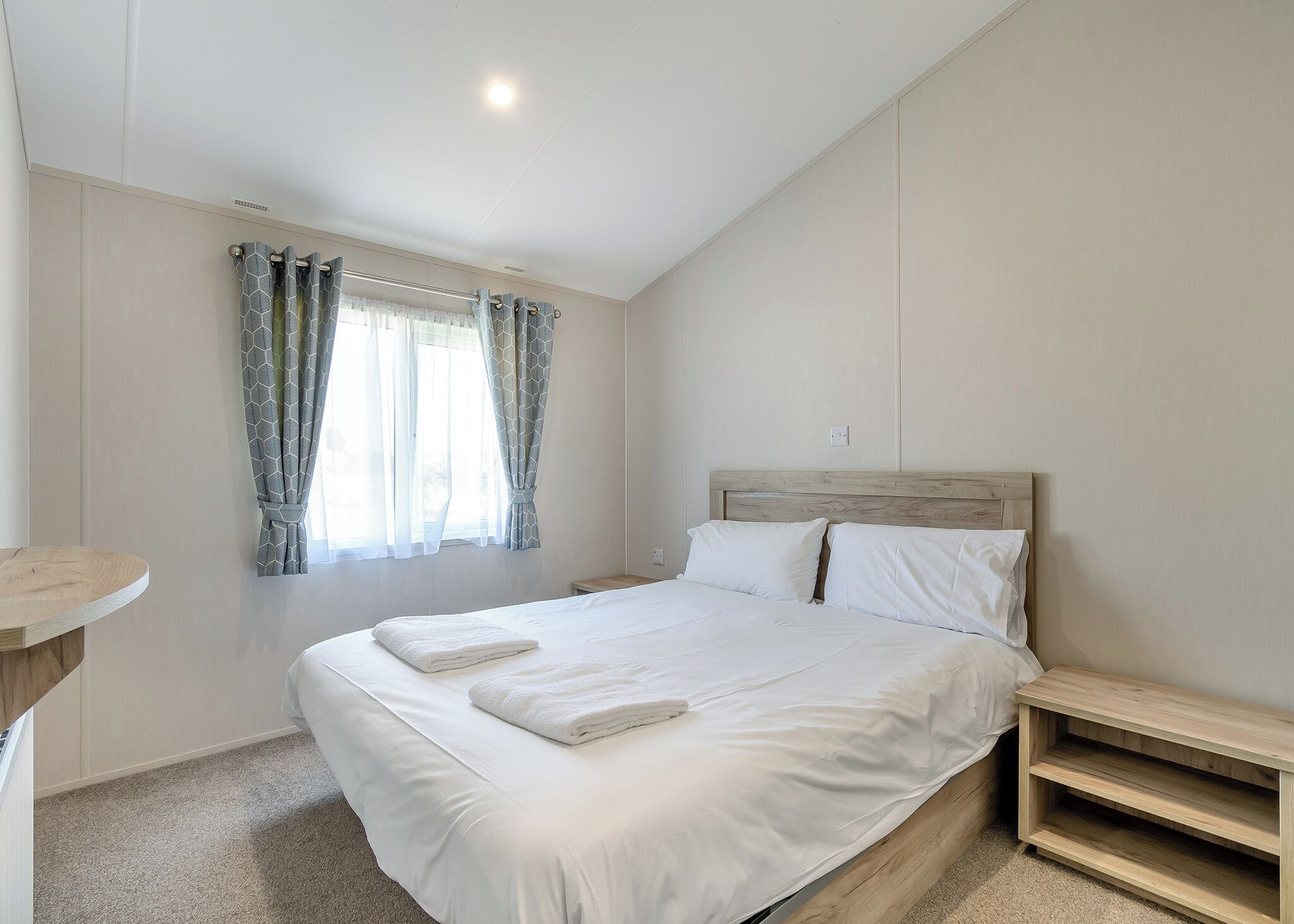 A bedroom with a bed, a bedside table, a nightstand, a window with curtains, and a light fixture.