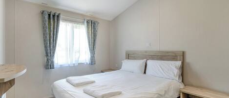 Une chambre à coucher comprenant un lit, une table de chevet, une commode, une fenêtre avec des rideaux et un luminaire.