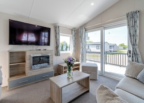 Ein Wohnzimmer mit Fernseher, Kamin, Sofa und Blick ins Freie.