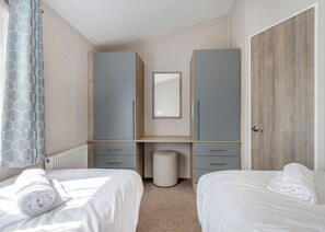 Quarto com duas camas, um guarda-roupa, um espelho e uma porta.