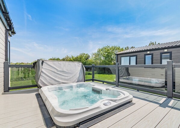 A hot tub on a wooden deck with a view of a house and greenery.