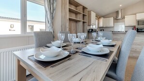 Un comedor moderno con una mesa larga dispuesta para seis comensales, armarios de madera y vistas del cielo a través de amplios ventanales.