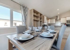A modern dining area with a long table set for six, wooden cabinets, and a view of the sky through large windows.