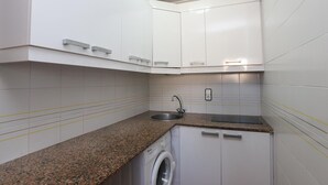 Una cocina compacta con armarios blancos, encimera de granito, lavadora y lavaplatos.