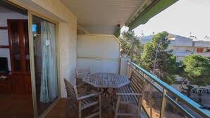 Un balcón con mesa y sillas de madera, un ventanal corredero y vistas del barrio circundante.