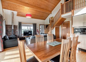 A modern living room with a wooden ceiling, a dining table, and a kitchen area.