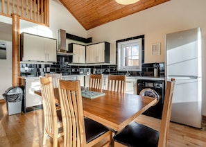 A modern kitchen with wooden chairs, a dining table, a built-in oven, and a refrigerator.