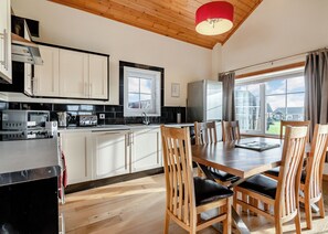 A modern kitchen with white cabinets, a dining area with wooden chairs, and a large window offering a view of the outside. - Outstanding, spacious and contemporary two storey lodge. (Hornsea)