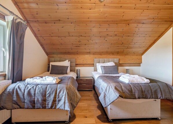 A bedroom with two beds, wooden ceiling, and a window with curtains.